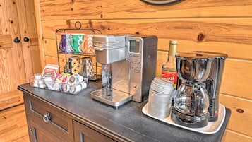 Een koffiehoek met een koffiezetapparaat, een stapel wegwerppmokken, een Coca-Cola fles en een koffiekan op een houten toonbank.