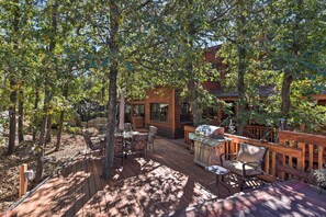 Une terrasse en bois avec des meubles d’extérieur, un barbecue et une vue sur un chalet.