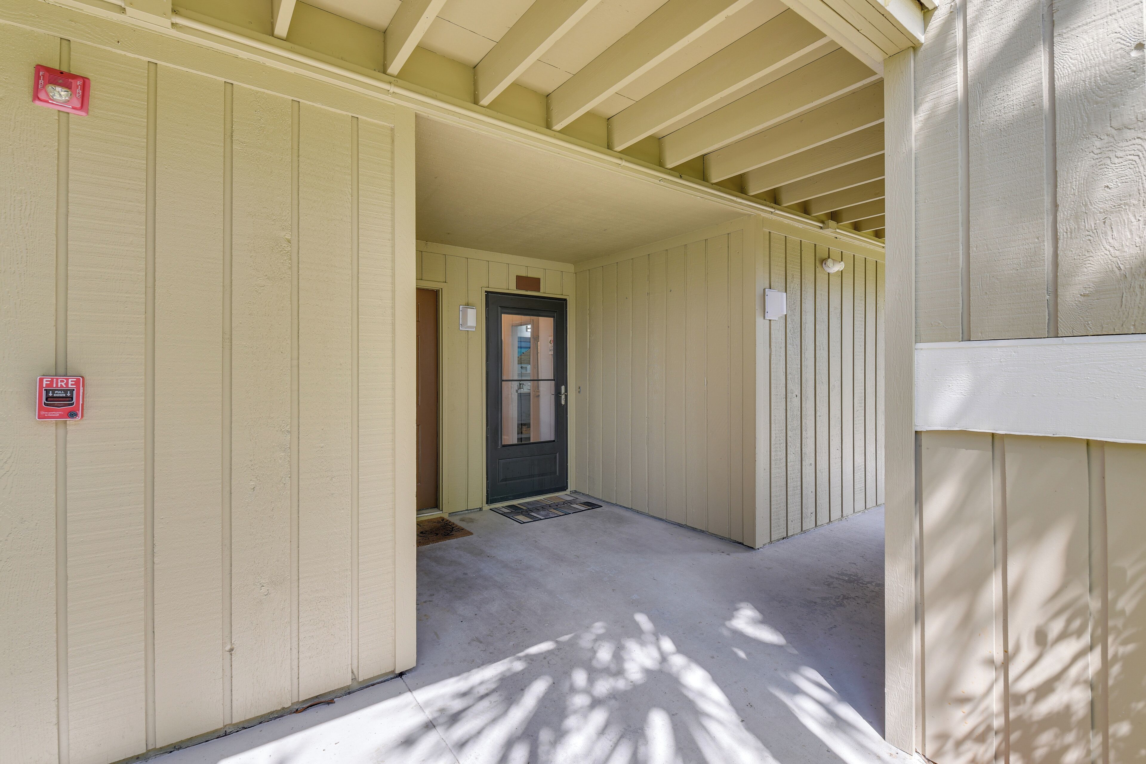 A hallway with a door leading to a room, a fire alarm, and a window.