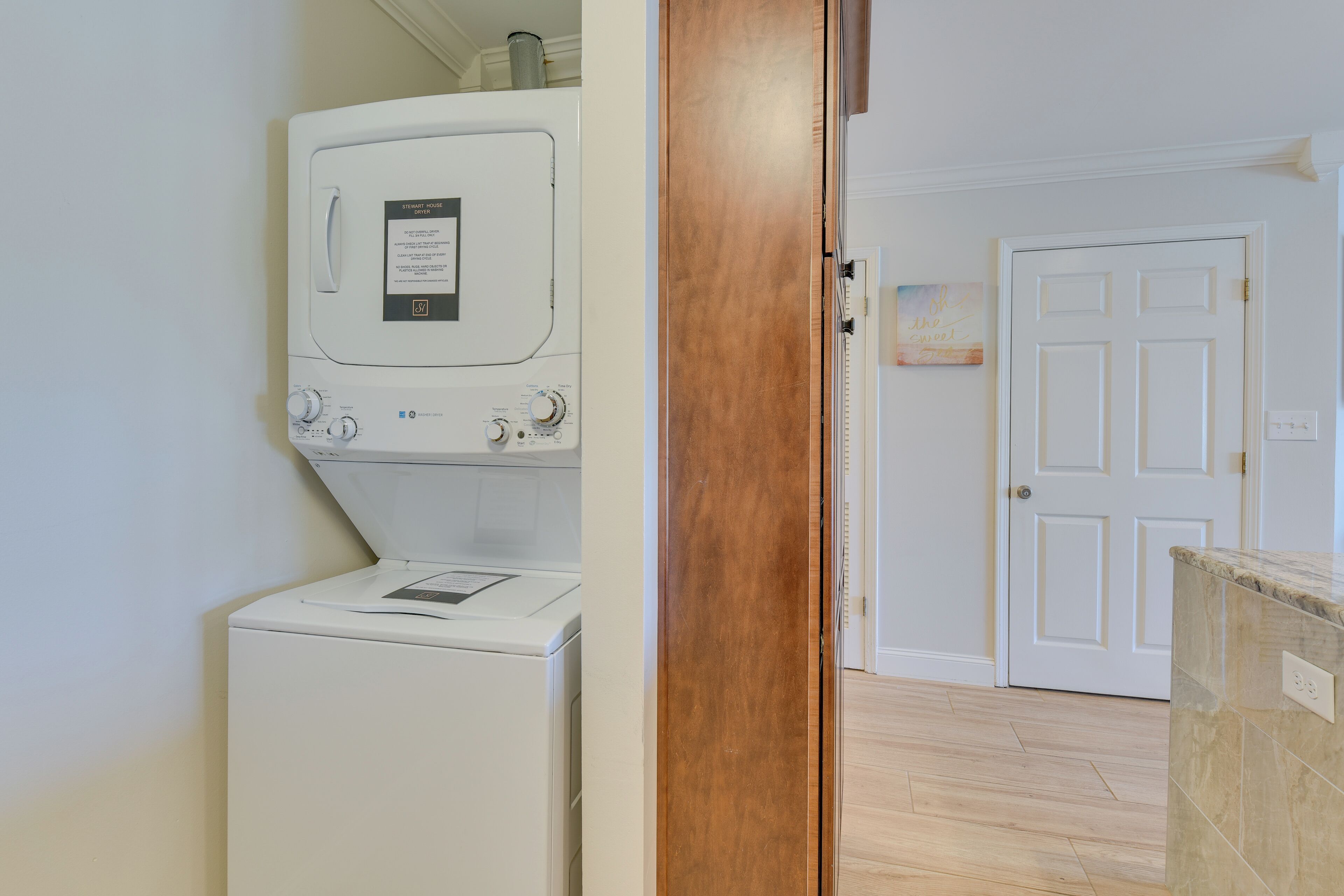A laundry room with a front-loading washer and dryer, a wooden door, and a white door in the background.