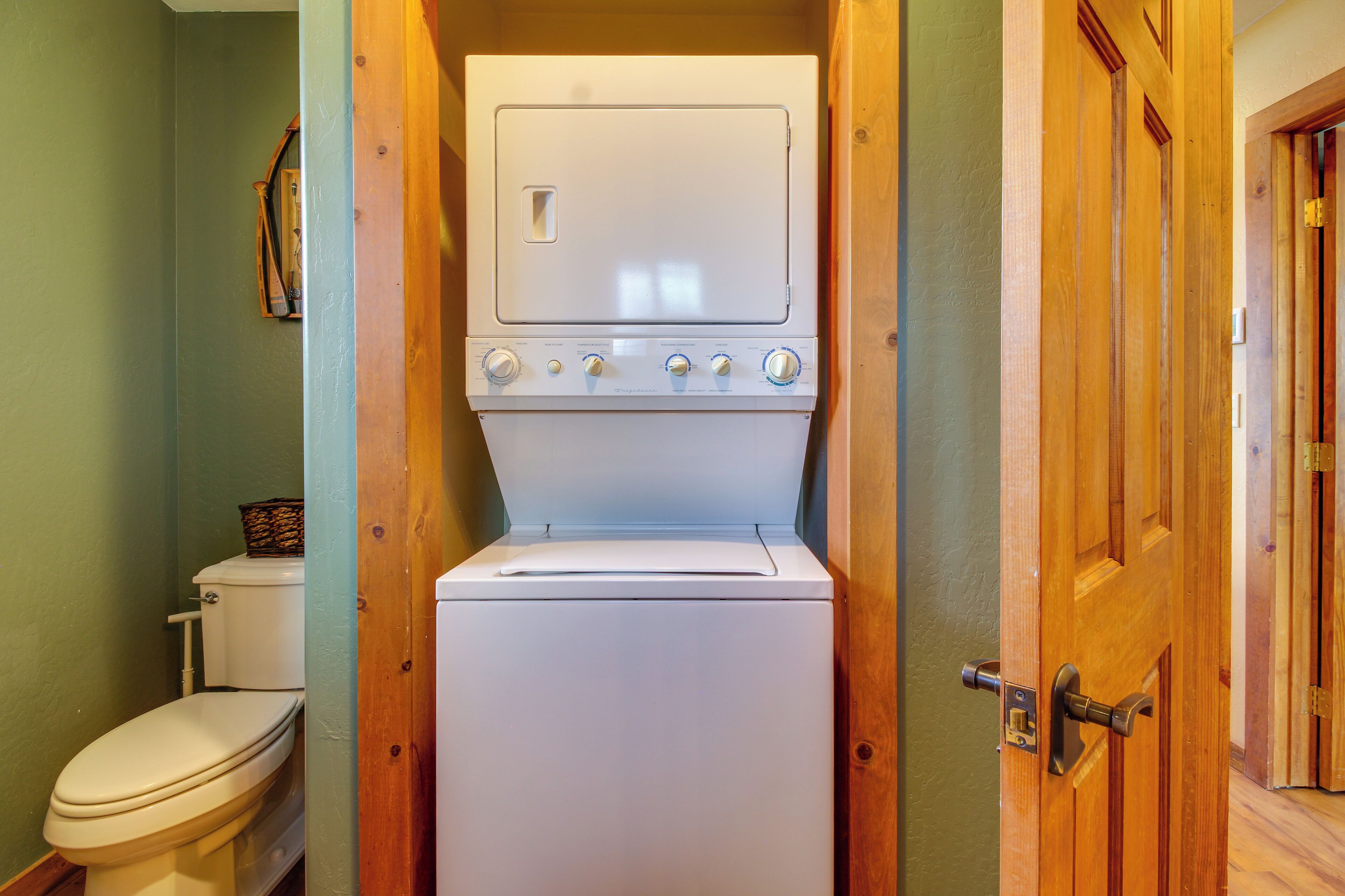 A compact laundry room with a washer and dryer, a toilet, and a wooden door.