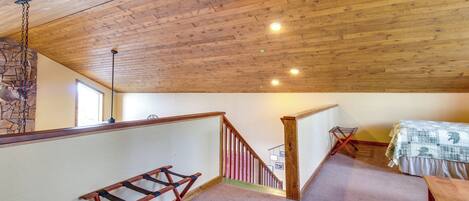 Une pièce avec un plafond en bois, un lit, un bureau, un escalier et un mur en pierre.