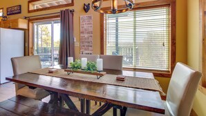 Un espace repas comprenant une table en bois, des chaises rembourrées, un lustre et une vue dégagée grâce à de grandes fenêtres.