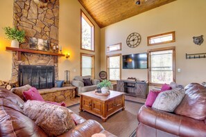 A spacious living room with a stone fireplace, leather sofas, a wooden coffee table, and a television.