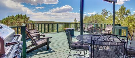 A covered outdoor deck with a grill, seating, and a view of the surrounding landscape.