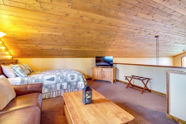 Een gezellige kamer met een bed, een houten plafond, een televisie en een klein tafeltje.