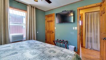 Un dormitorio con cama, ventilador de techo, televisor y ventana con cortinas.