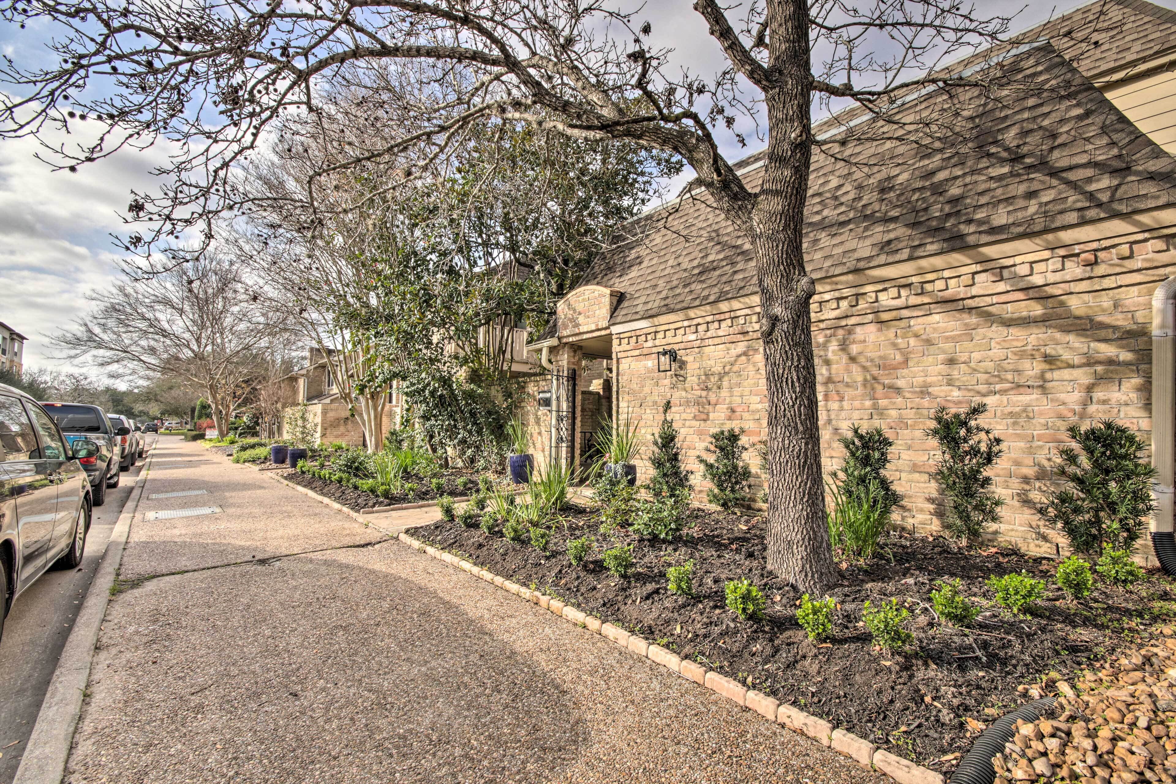 Une rue résidentielle bordée de maisons en briques, d’un trottoir planté d’arbres et de voitures garées.