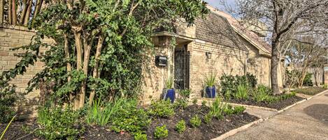 A stone building with a brick facade, a small garden with various plants, and a metal gate.
