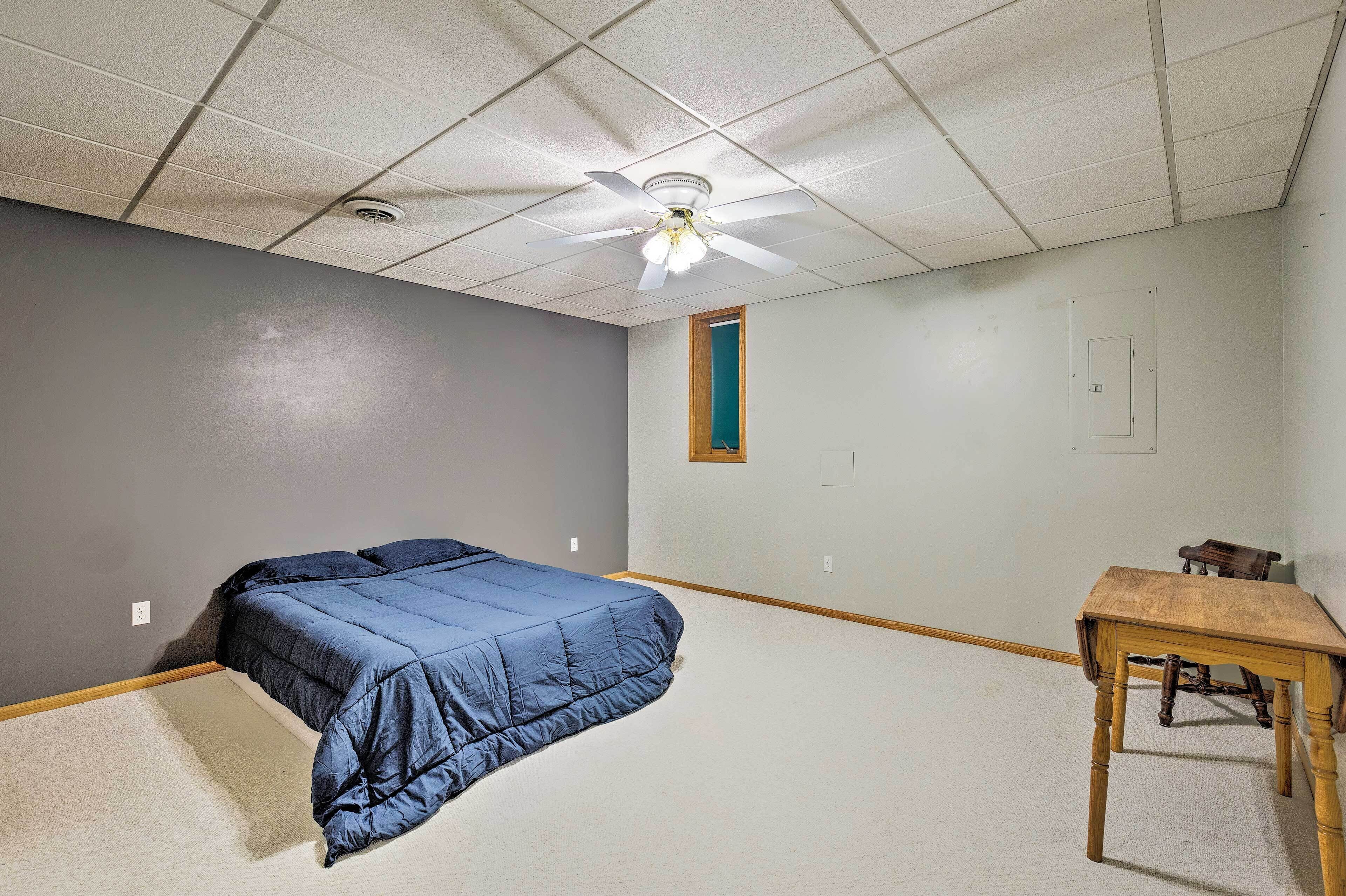 A bedroom with a bed, a ceiling fan, a small table, and a window.