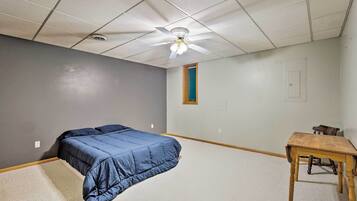 A bedroom with a bed, a ceiling fan, a small table, and a window.