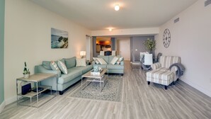 A modern living room with a sofa, armchair, coffee table, and a dining area in the background. - Luxurious Daytona Beach Condo w/ Resort Amenities! (Holly Hill)