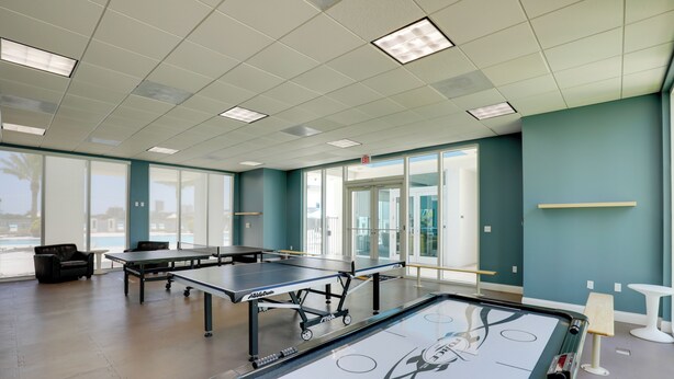 A spacious indoor area with ping pong tables and a foosball table, large windows, and a teal-colored wall. - Luxurious Daytona Beach Condo w/ Resort Amenities! (Holly Hill)