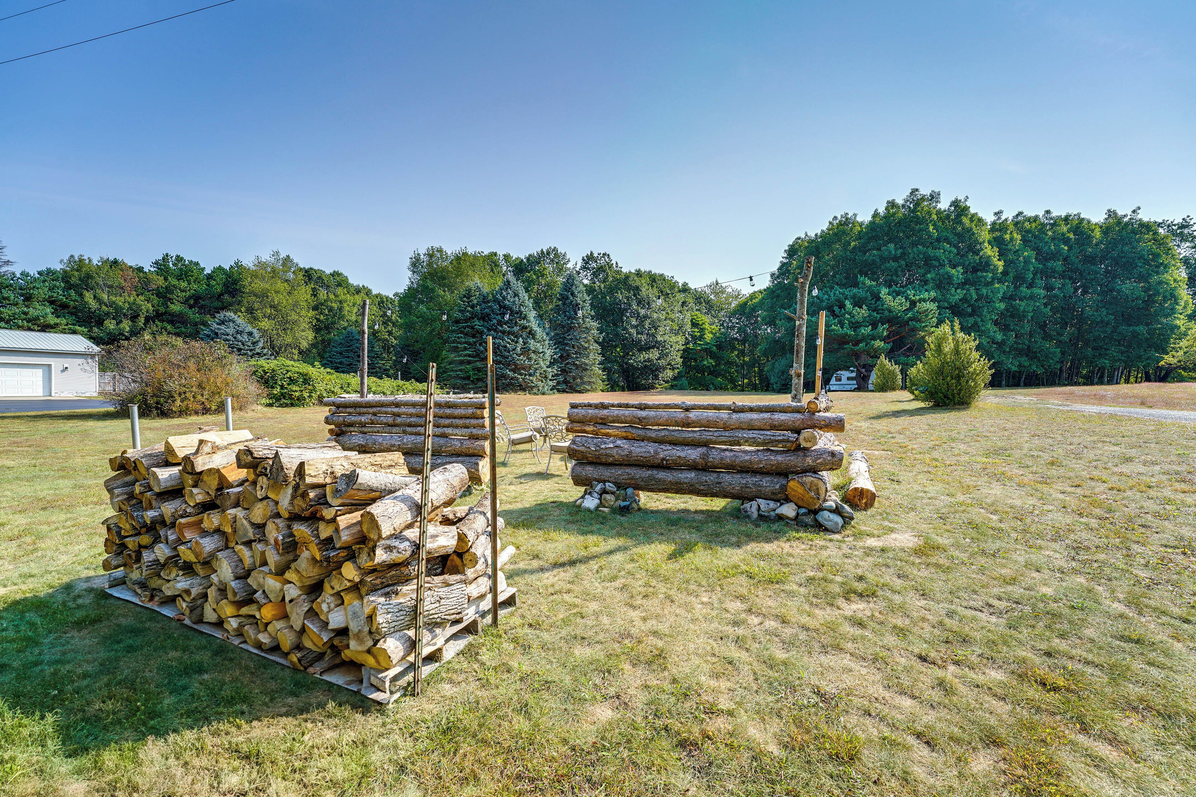 Une pile de bois de chauffage dans un champ herbeux, avec des arbres en arrière-plan.