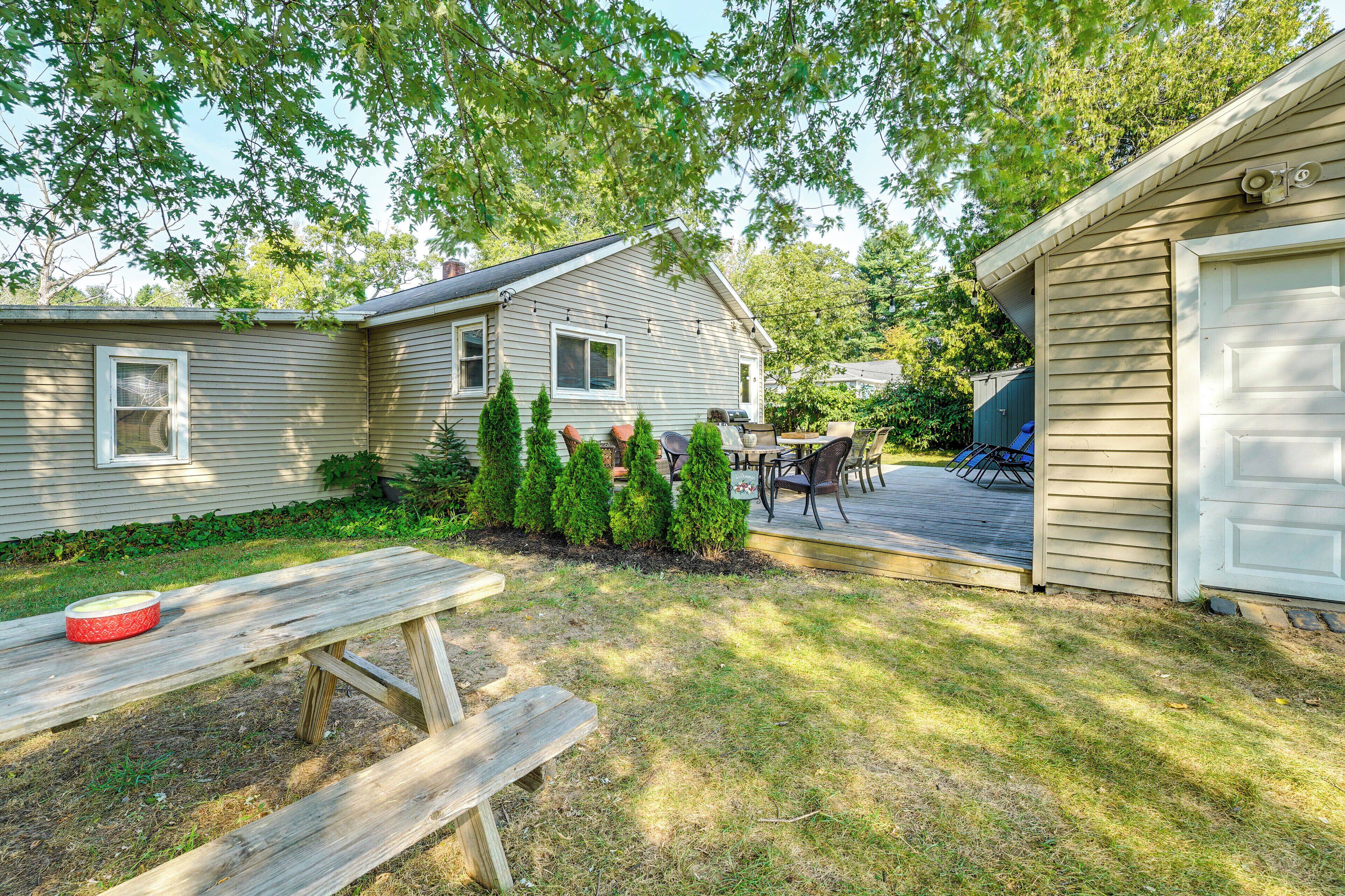 A backyard with a wooden picnic table, a barbecue grill, and a covered patio area.