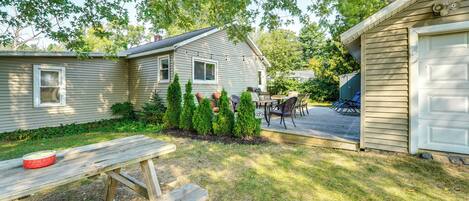 A backyard with a wooden picnic table, a barbecue grill, and a covered patio area.