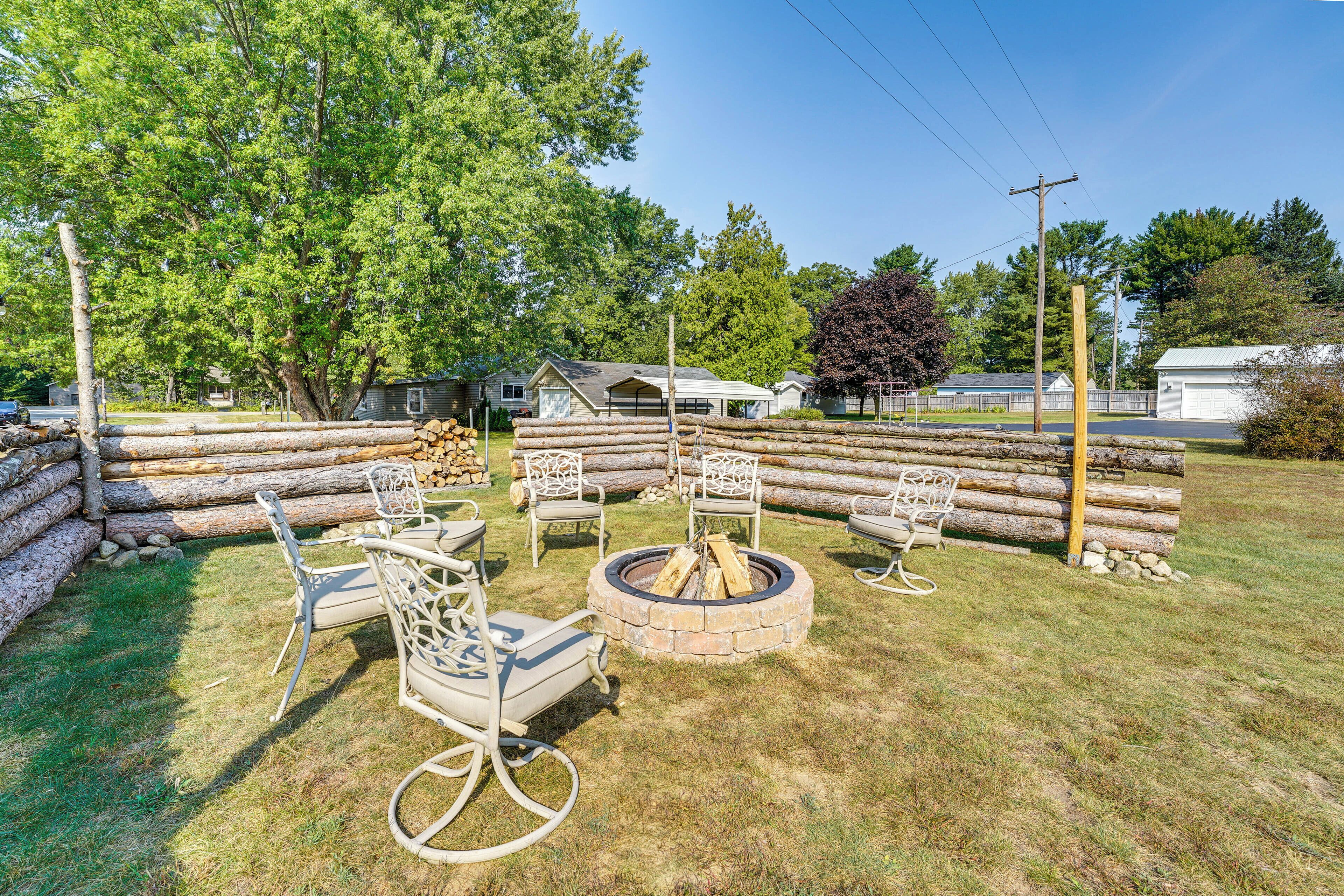 A backyard with a fire pit, outdoor furniture, and stacked firewood.