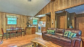A wooden-paneled living room with a leather sofa, dining table, chairs, and a kitchen area in the background. - Home in Big Bass Lake Community: Fire Pit & Grill! (Gouldsboro)