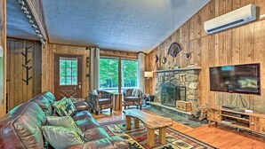 A cozy living room with a leather couch, wooden coffee table, and a stone fireplace. - Home in Big Bass Lake Community: Fire Pit & Grill! (Gouldsboro)