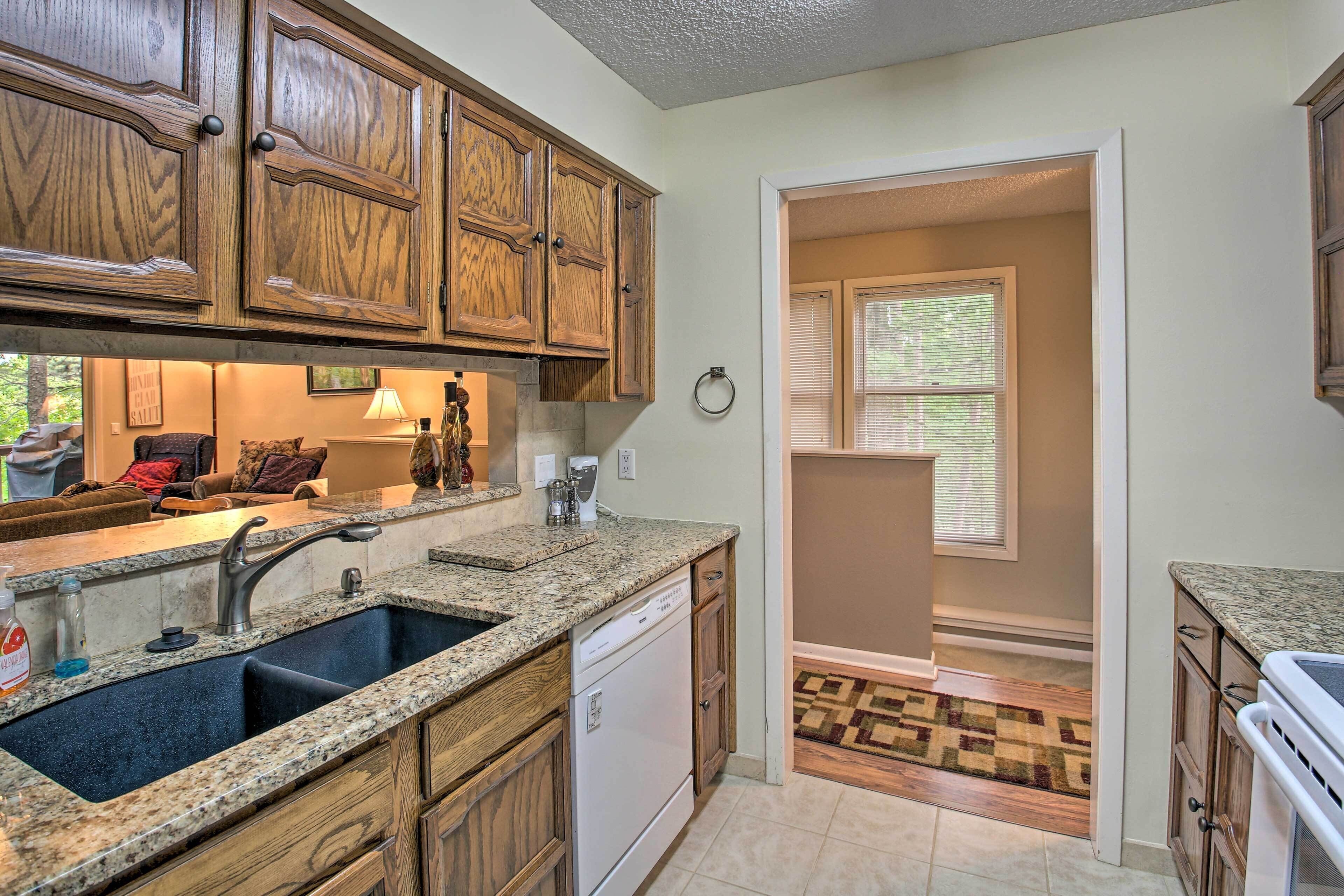 A kitchen with granite countertops, wooden cabinets, a dishwasher, and a window with blinds.