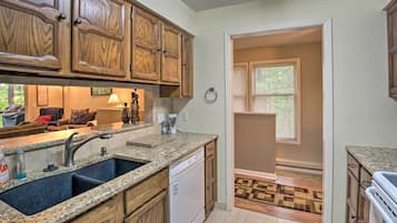 A kitchen with granite countertops, wooden cabinets, a dishwasher, and a window with blinds.