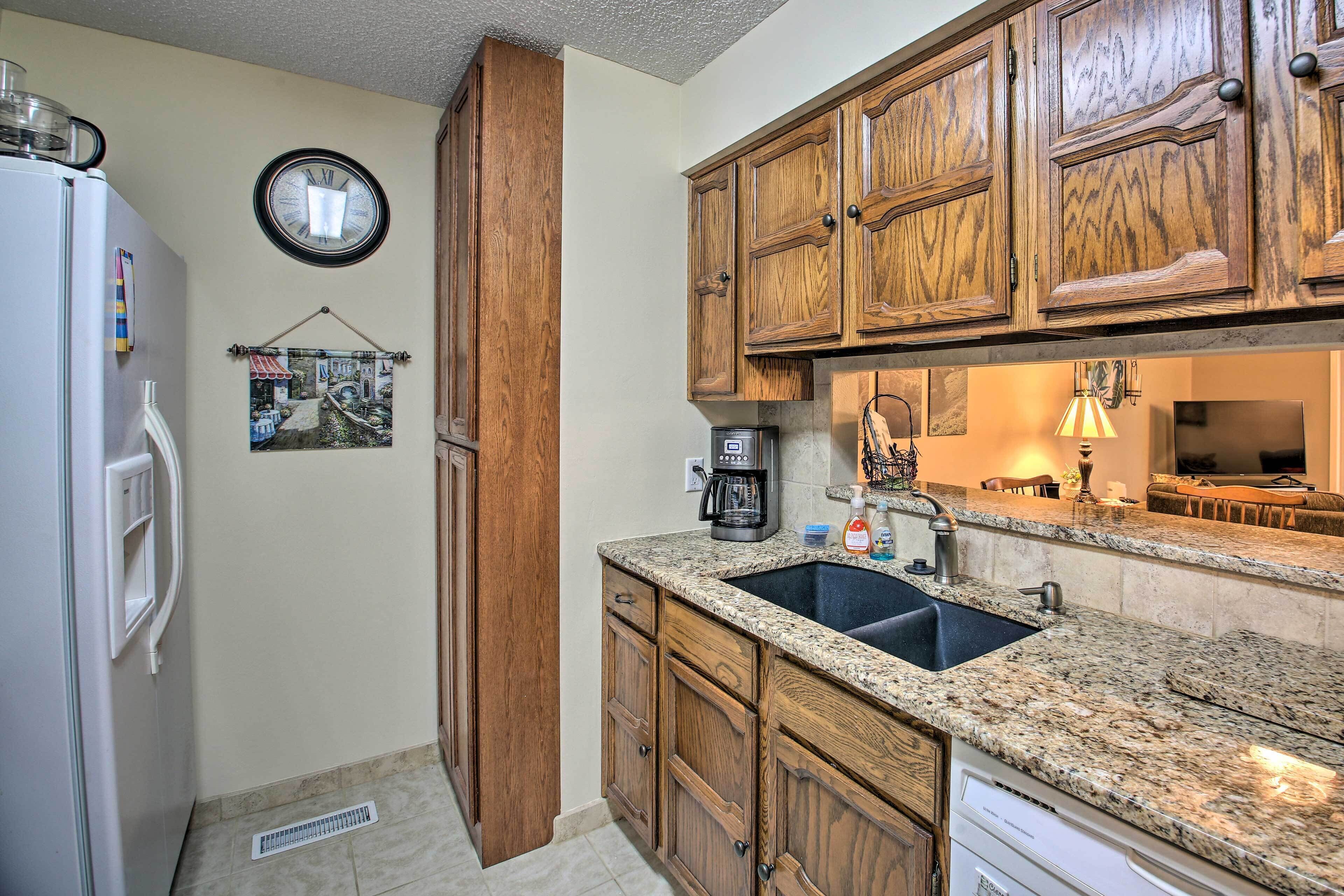 A kitchen with wooden cabinets, a granite countertop, a sink, a coffee maker, and a clock on the wall.