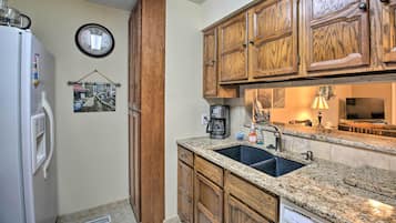 A kitchen with wooden cabinets, a granite countertop, a sink, a coffee maker, and a clock on the wall.