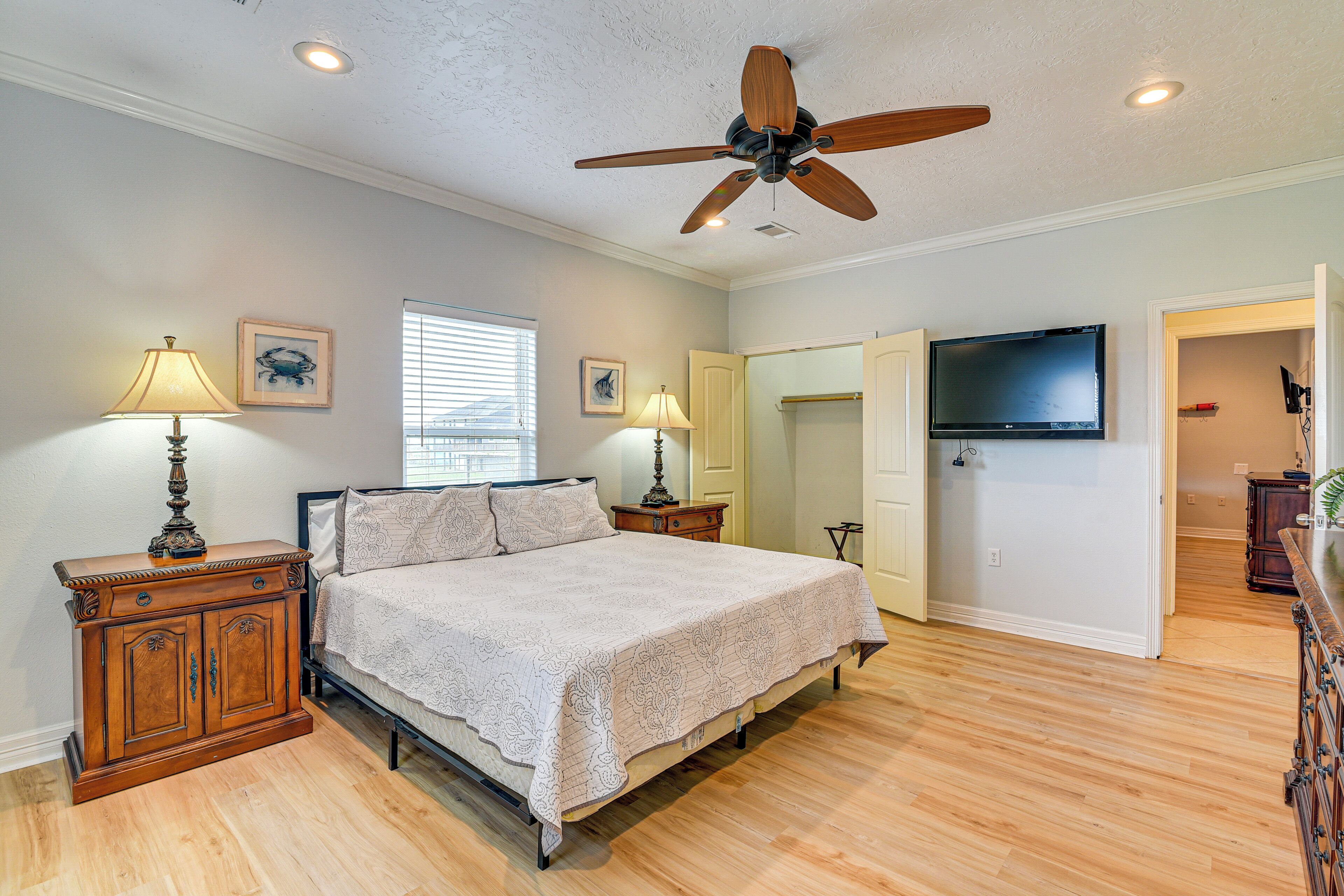 A bedroom with a bed, two nightstands, a ceiling fan, a TV, and a door leading to another room.