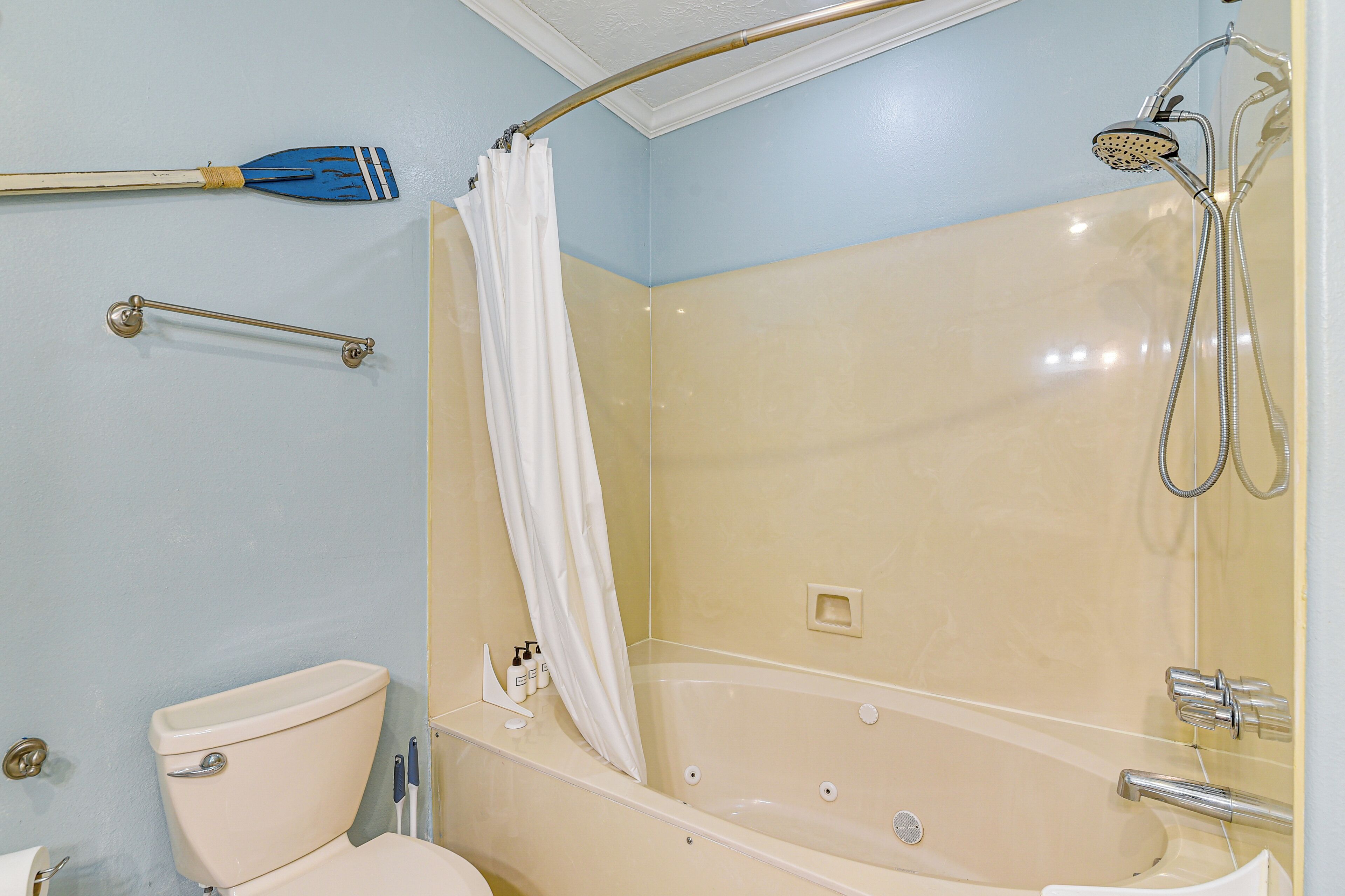 A bathroom with a bathtub, shower, toilet, and handrails.