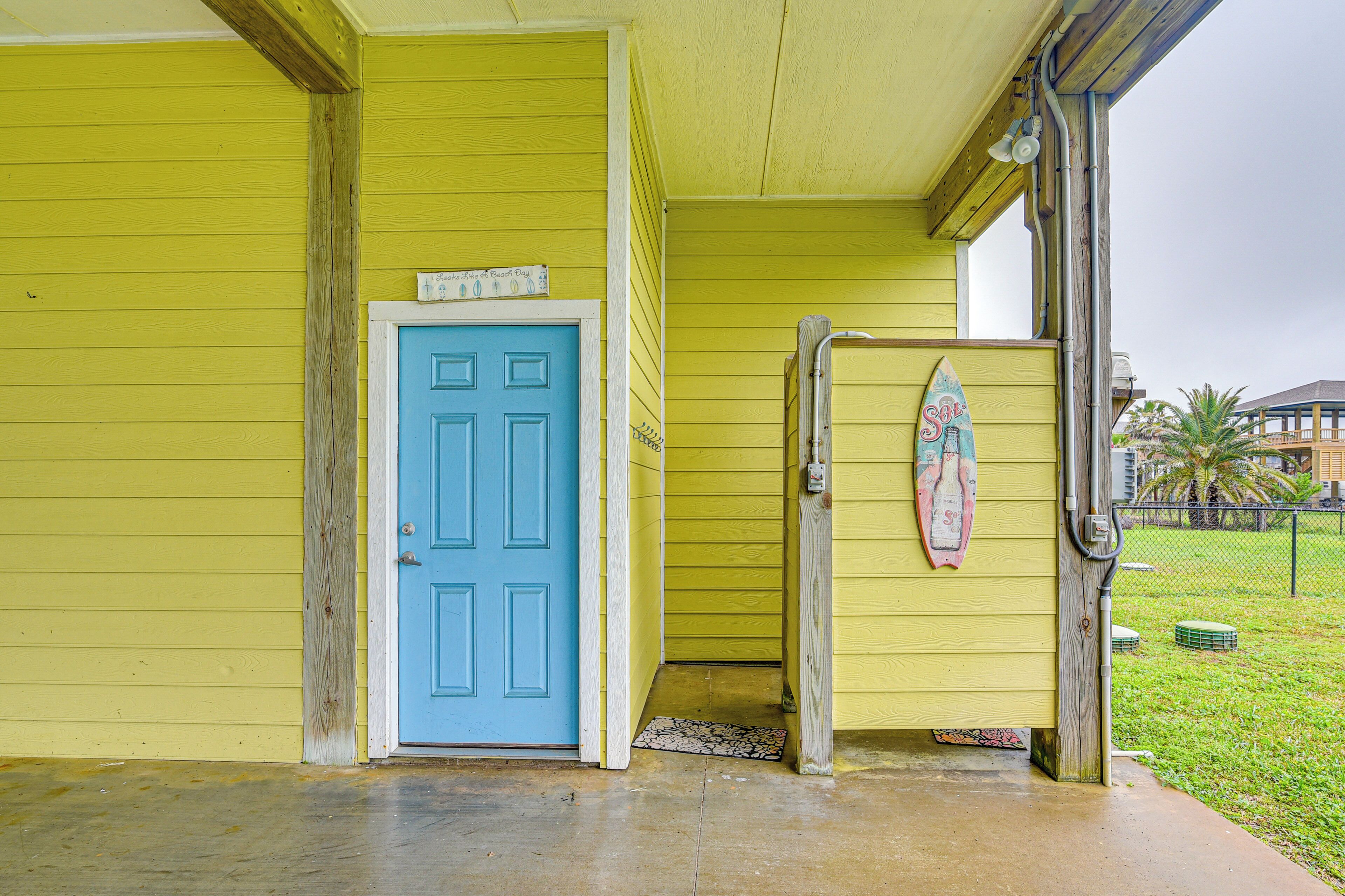 Un bâtiment jaune avec une porte bleue et une planche de surf accrochée au mur.