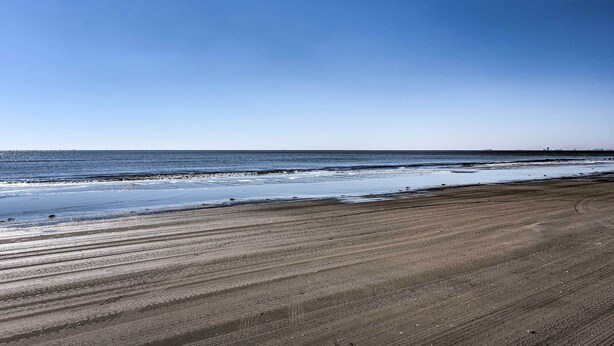 Ein Strand mit weitem Sandufer und ruhigem Wasser.