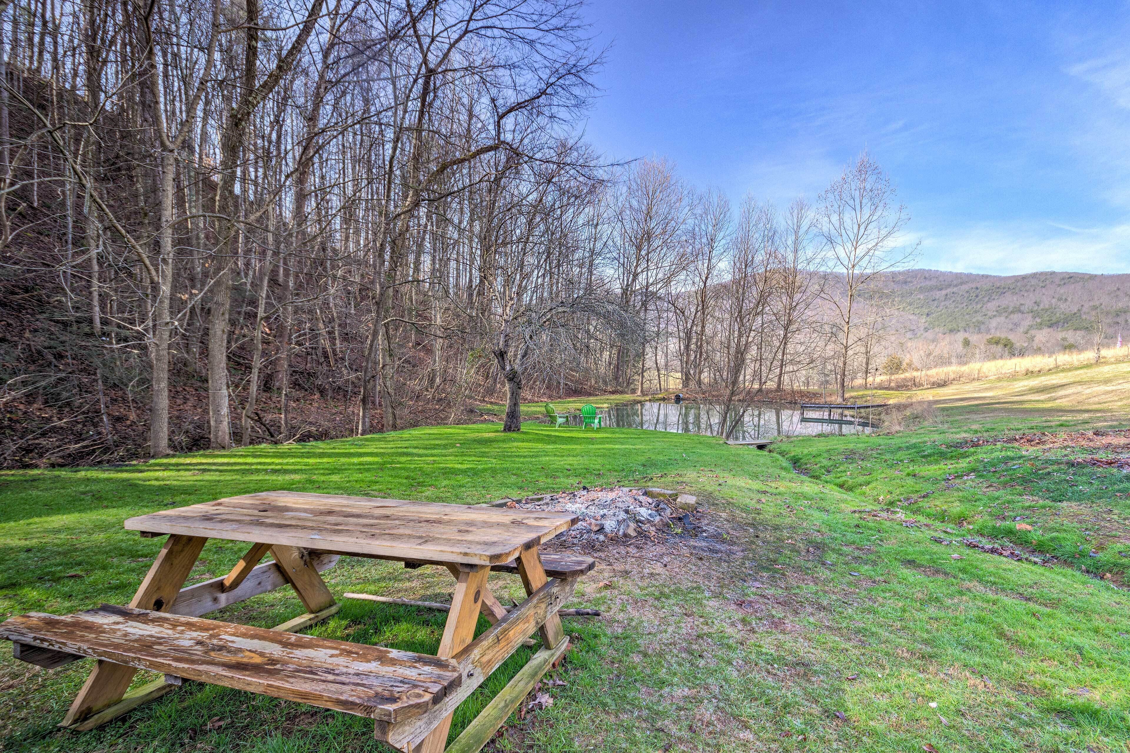 A picnic table in a grassy area with a pond and trees in the background.