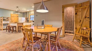 A dining area with a round wooden table, four wooden chairs, a hanging pendant light, and a patterned rug.