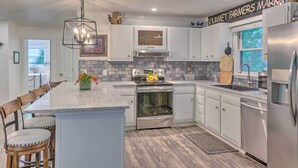 A modern kitchen with white cabinets, a central island, a stainless steel refrigerator, and a backsplash. - Beautiful Connestee Falls Home w/ Porch in Brevard (Brevard)