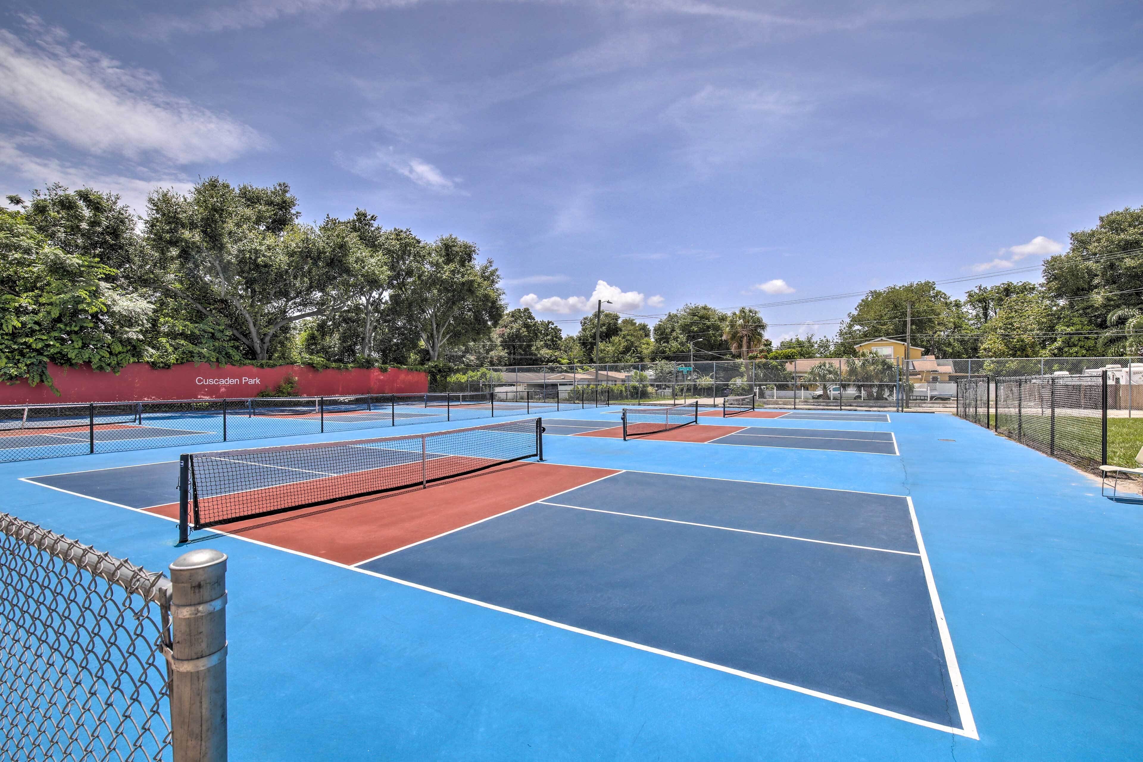 An outdoor tennis court with multiple courts, a chain-link fence, and a red wall with "Cascades Park" written on it.
