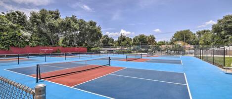 An outdoor tennis court with multiple courts, a chain-link fence, and a red wall with "Cascades Park" written on it.