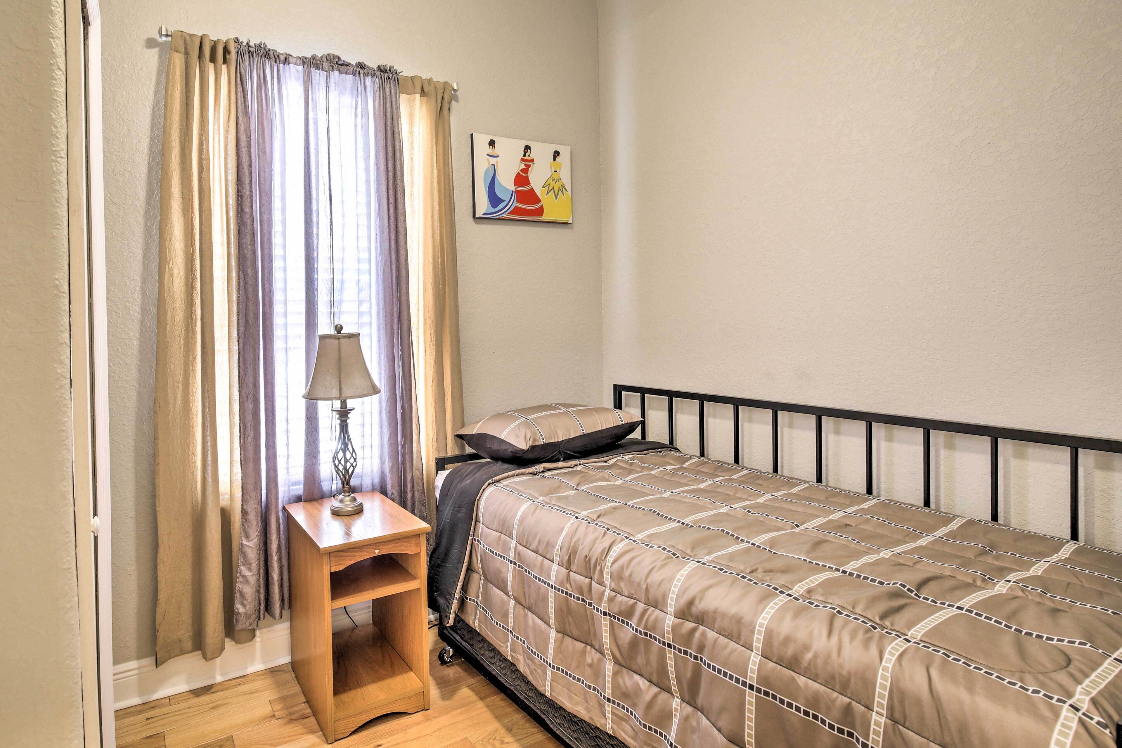 Un dormitorio con cama, mesita de noche, lámpara y un cuadro en la pared.