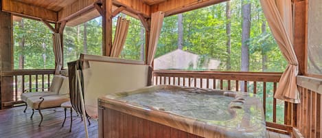 A wooden deck with a hot tub, a chair, and a view of the forest.