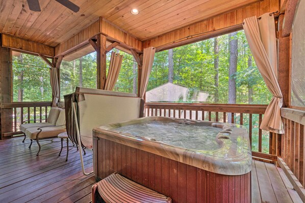 A wooden deck with a hot tub, a chair, and a view of the forest.