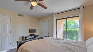 Une chambre avec un lit, un ventilateur de plafond, une télévision et une porte-fenêtre coulissante donnant sur l’extérieur.
