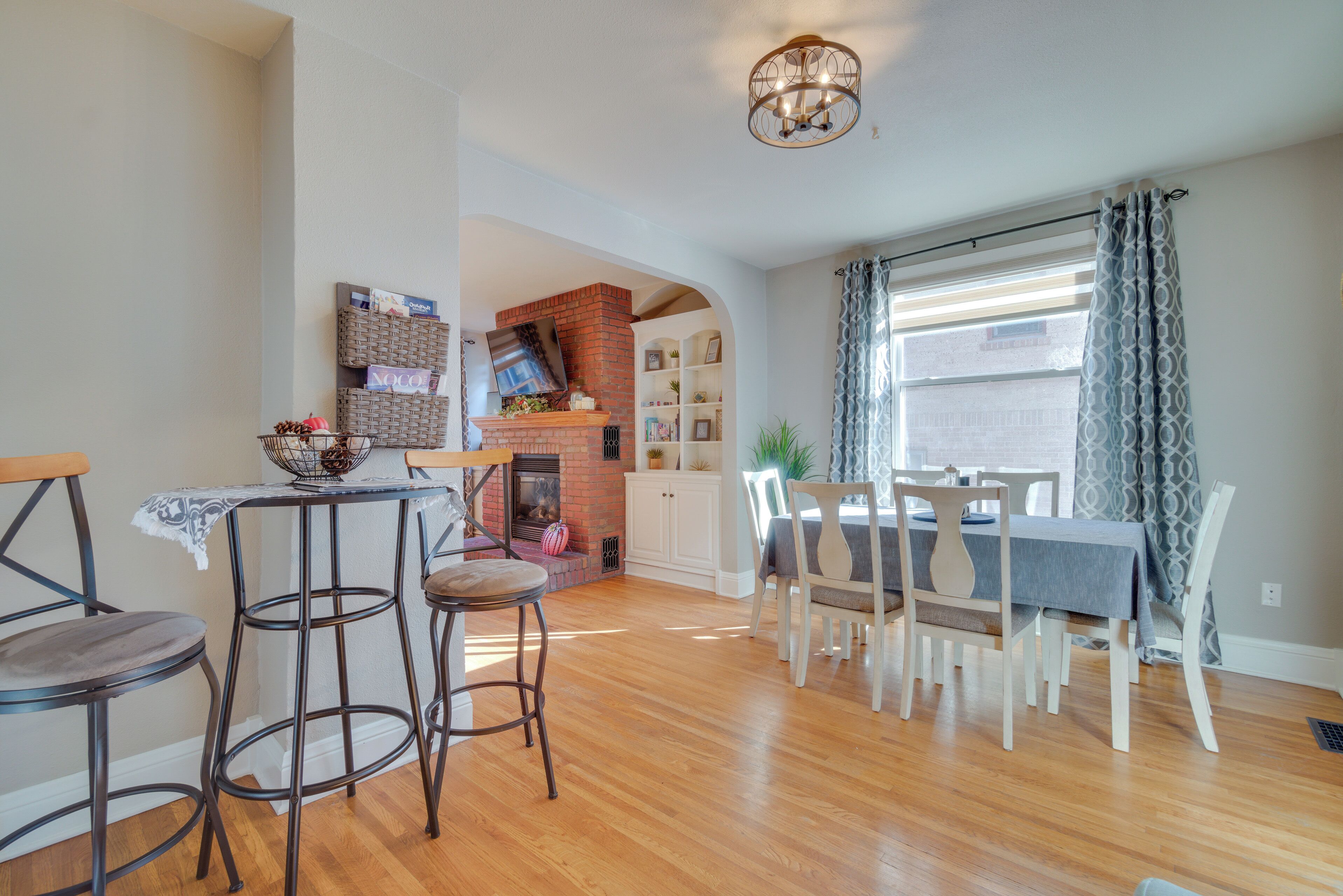 A dining area with a brick fireplace, a table with chairs, and a window with curtains.