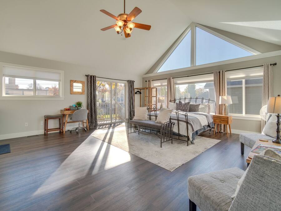 A spacious living room with a high ceiling, large windows, and a ceiling fan.