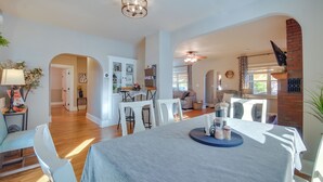 A spacious dining area with a high ceiling, a chandelier, and a brick fireplace. There are white chairs and a table with a blue tablecloth. - Charming Getaway, Walk to Windsor Lake & Downtown! (Windsor)