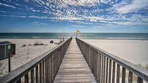 Ein Holzsteg führt zu einem Strand mit einer Flagge.