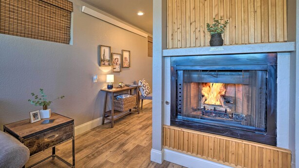 A cozy living room with a fireplace, wooden paneling, and a small table with a lamp.