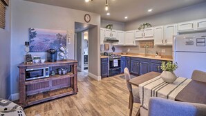 A modern kitchen with white cabinets, a built-in oven, and a refrigerator. There is a dining area with a table and chairs, and a wooden cabinet with kitchen appliances.