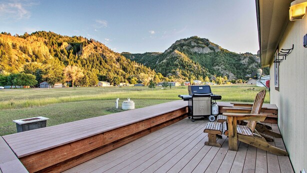 Une terrasse avec un barbecue et des chaises, donnant sur une pelouse et des montagnes.