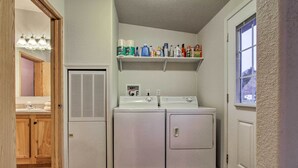 Une buanderie équipée de deux machines à laver, d’un sèche-linge et d’étagères où sont rangés divers produits de nettoyage.