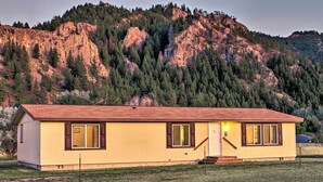 Il s’agit d’un bâtiment jaune à un seul étage, doté d’un toit rouge, de volets bruns et d’un porche à l’avant. Il est situé dans une zone herbeuse, avec une chaîne de montagnes en arrière-plan.