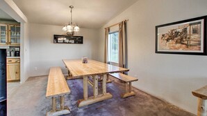 Un coin repas avec une table et des bancs en bois, un lustre, un tableau encadré au mur et une fenêtre avec des rideaux.